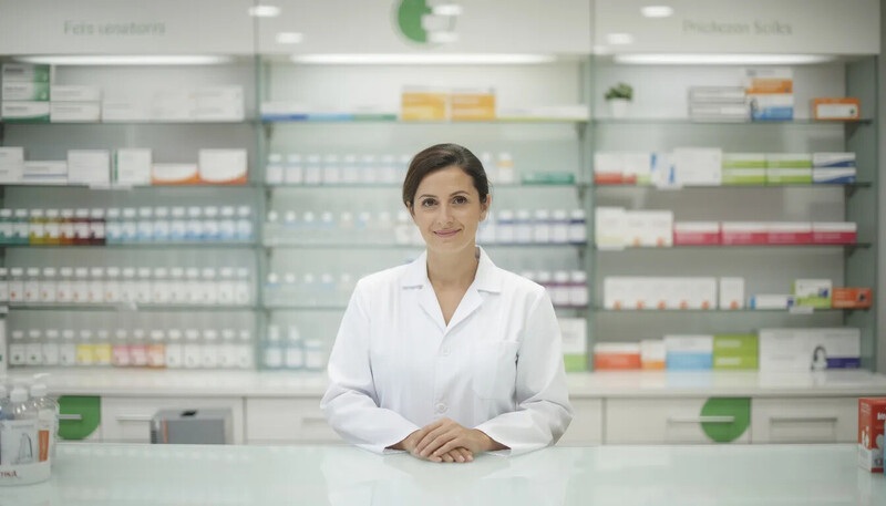 Un pharmacien en blouse blanche se tient dans une officine moderne, entouré d'étagères remplies de médicaments. Il incarne le professionnalisme du métier de pharmacien, prêt à offrir conseils et expertise aux patients.