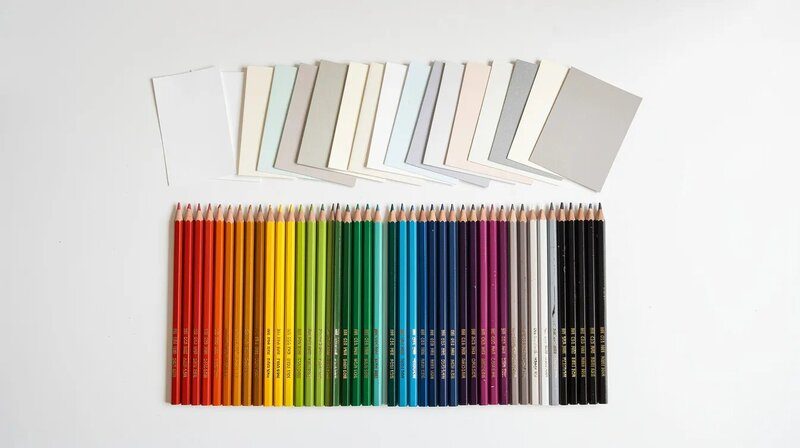 Sur un bureau blanc, des crayons de couleur et des échantillons de papier sont soigneusement disposés, illustrant un choix de couleurs varié pour la création de modèles de CV modernes. Cette mise en page colorée évoque la créativité et l'importance du design dans la rédaction de candidatures professionnelles.